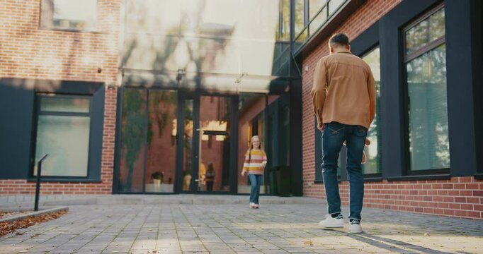 Beautiful Caucasian girl with glasses leaving school. Coming to her dad and smiling. Parent gifting soft toy to child. Giving high five to each other. Getting ready for trip back home.