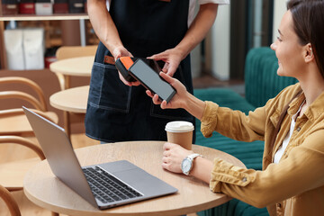 Woman paying with smartphone via terminal at wooden table in cafe