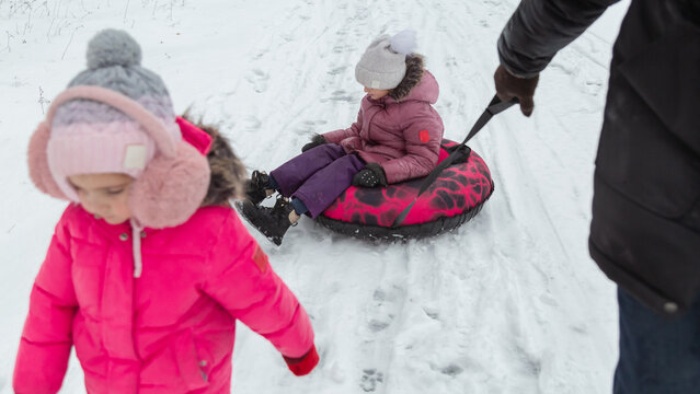 Father and daughters ride downhill on a Snow tubing in the park on the winter holidays
