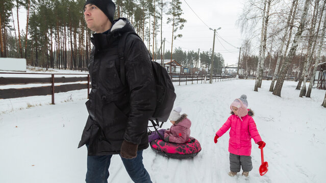 Father and daughters ride downhill on a Snow tubing in the park on the winter holidays