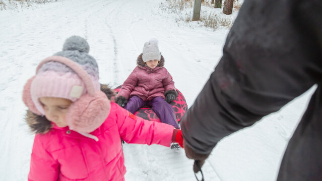 Father and daughters ride downhill on a Snow tubing in the park on the winter holidays