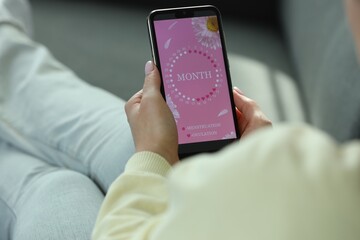 Menstruation. Woman using period calendar application on smartphone indoors, closeup