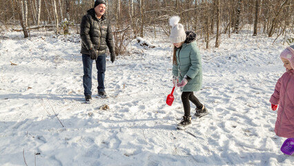 Little girls play with snow with her grandfather in winter forest