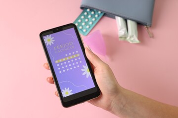 Menstruation. Woman holding smartphone with period calendar application on pink background, above view