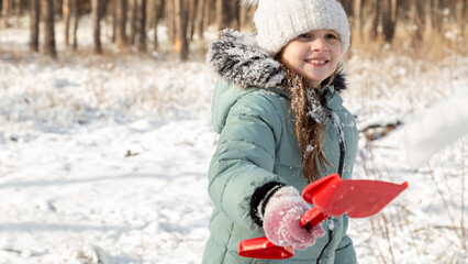 Cheerful positive child girl wearing a outerwear smiling walking through a snowy countryside forest