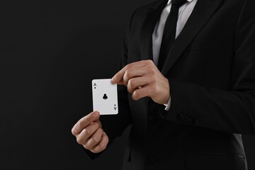 Illusionist showing playing card on black background, closeup. Space for text