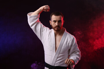 Man wearing uniform practicing karate in color lights and smoke against black background
