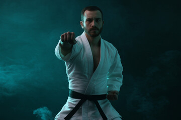 Karate fighter wearing uniform in color lights and smoke
