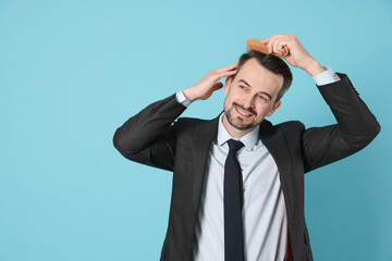 Handsome man stylish his hair with comb on light blue background