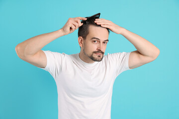Fototapeta premium Handsome man stylish his hair with comb on light blue background