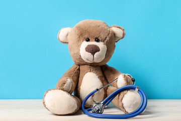 Pediatrics concept. Teddy bear with stethoscope on wooden table against light blue background