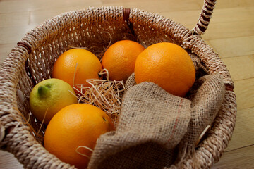 Juicy Oranges and One Lemon in a Straw Shavings in a Braided Basket on a Wood Table. Fruits Basket...