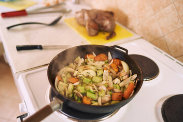Steam rises from chopped vegetables stewed in a frying pan on the stove