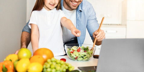 Online Recipes. Cute Father And Daughter Cooking Using Laptop Preparing Dinner Together In Kitchen...