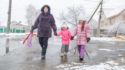 Grandmother and girls walk along a snowy street in winter