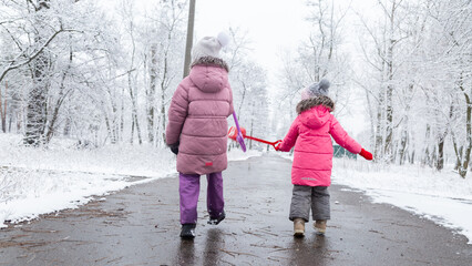Two little girls in colorful clothes play outdoors during a snowfall.