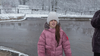 Girl in warm clothes playing outdoors in winter park, enjoying snowy weather.
