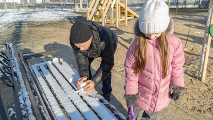 Grandfather with granddaughters making a little snowman in sunny winter day