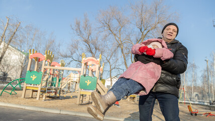 Grandfather playing with her granddaughter on the playground in the park in winter
