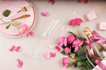 A stylish flat lay composition featuring pink plates, a champagne flute, a bottle of sparkling...