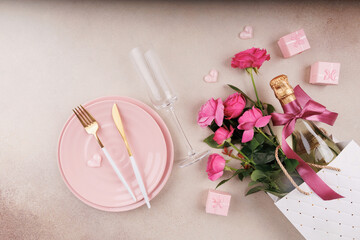 A stylish Valentine's Day table setting with pink plates, golden cutlery, champagne, pink roses, and romantic gift boxes.