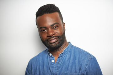 Portrait of a confident Black man in a denim shirt smiling against a white background  
