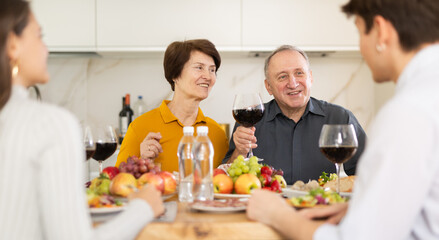 Senior man and woman sitting with their grown children during family holiday table in light kitchen