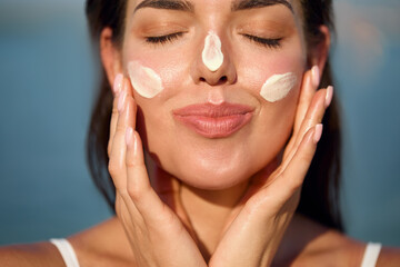 Beautiful young woman with sun cream on face. Girl applying sunscreen lotion on skin.Skin care. Sun...