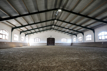 View in an indoor riding hall for horses and riders. The riding school is suitable for dressage and jumping horses.Empty riding arena is suitable for riders