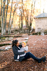 Fototapeta premium Mom looks at a little girl on her knees sitting on the ground in the autumn forest