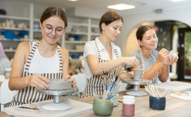 Young woman teacher and two girls students sculpt from clay and paint pottery