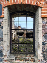 View of the old ruins of stones and bricks through a window opening with a black lattice. Old architecture with a history. Buildings and construction