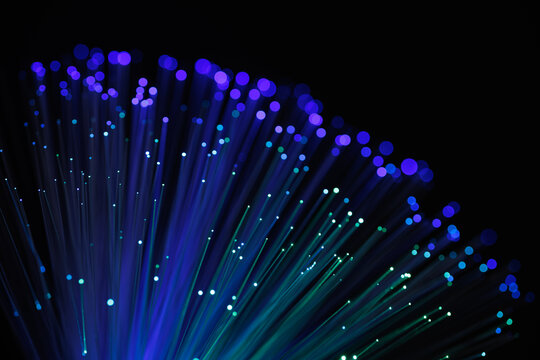 Glowing fiber optic cables with vibrant blue and purple bokeh lights on a dark background, representing fast internet, data transfer, and technology