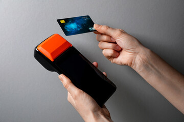 Woman with credit card using payment terminal on grey background, closeup