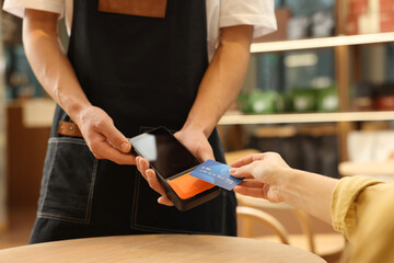 Woman paying with credit card via terminal at wooden table in cafe, closeup