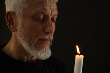Sad senior man with burning candle crying on black background. Grieving loss