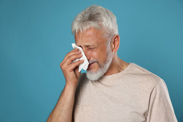Sad senior man crying on light blue background