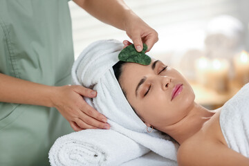 Young woman receiving facial massage with gua sha tool in spa salon