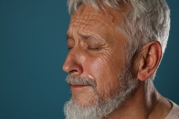Sad senior man crying on blue background, closeup