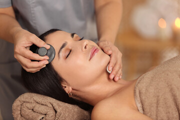 Young woman receiving facial massage with spa stone in salon