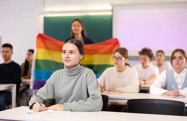 Fototapeta na wymiar Students study in classroom, teacher stands behind with rainbow flag