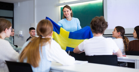 Confident young female professor shows students flag of Sweden