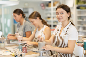 During working day, three employees of pottery workshop molding from clay, paint finished product. They apply pattern to surface of plate with brush, smoothing surface, carry out order at work table