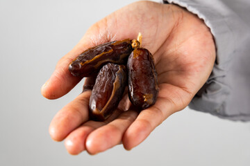 A person wearing a grey sleeve holds a bunch of fresh dates against a white backdrop