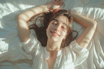 Fototapeta premium Dreaming girl lying on white bed with big pillows, spreading elbows to stretch arms, not willing to wake up fast, enjoying free time at weekend