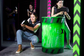 Laser tag players cheerful positive smiling girls playing in teams in dark laser tag room