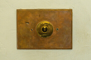 Close up of antique toggle light switch with copper faceplate on textured concrete wall providing vintage, rustic design detail.