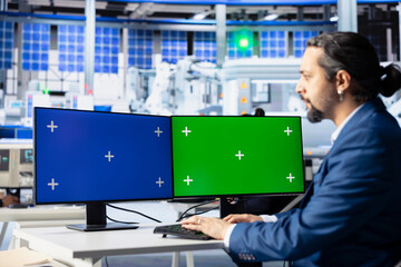 Engineer in photovoltaics factory reviewing system logs on isolated screen computer displays to...