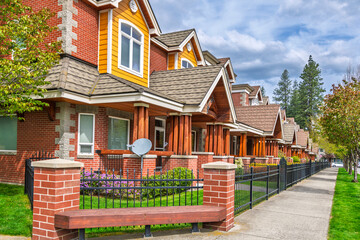A row of luxury townhomes with fenced front gardens on a suburban street.