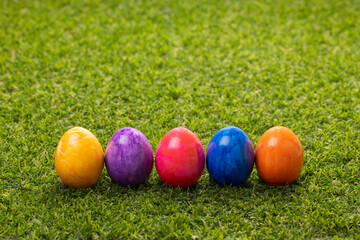 Five multi-colored Easter eggs stand in a row on the lawn